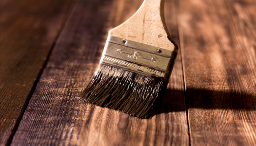 Up close image of a brush painting wood with a dark stain